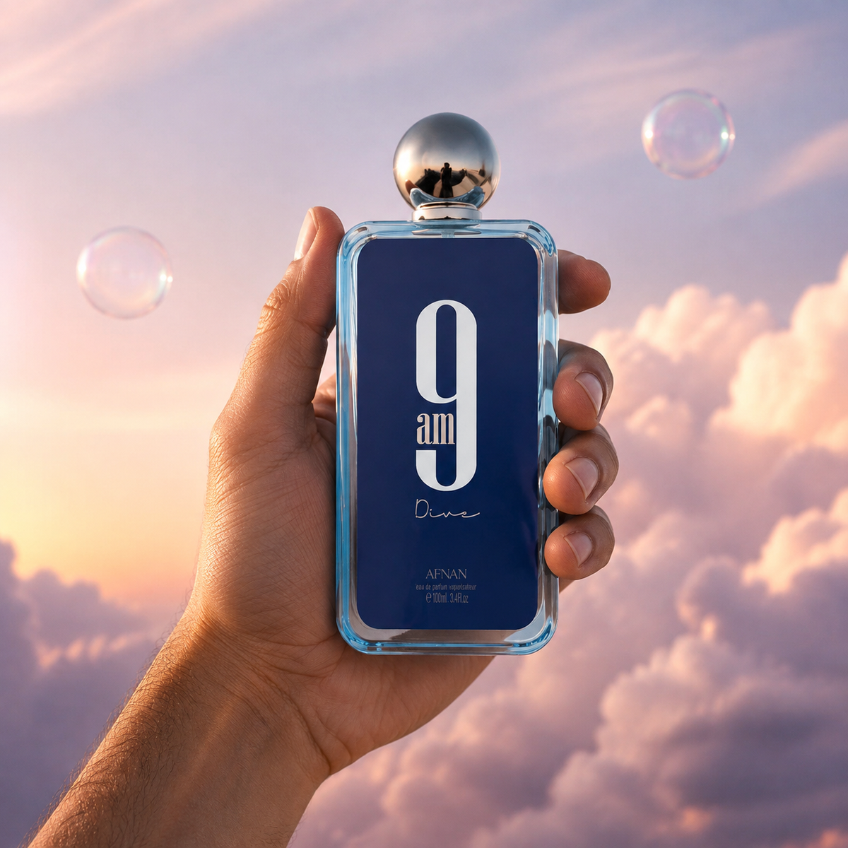 A hand holds the bottle of 9 AM Dive by Afnan among pink clouds.