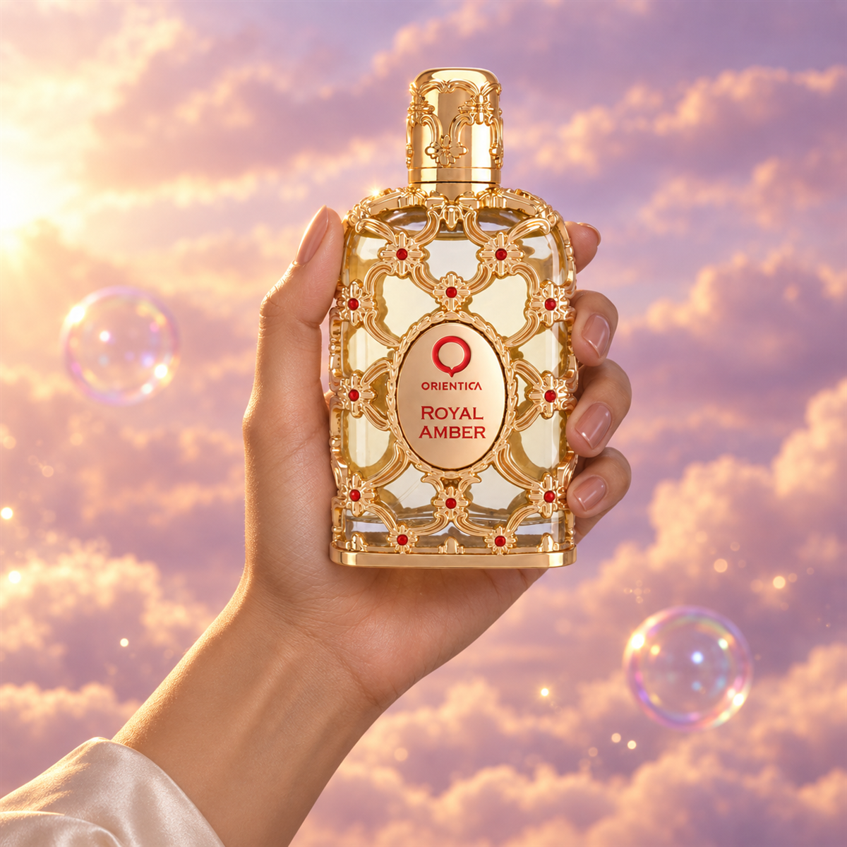 A hand holds the bottle of Royal Amber by Orientica among pink clouds.