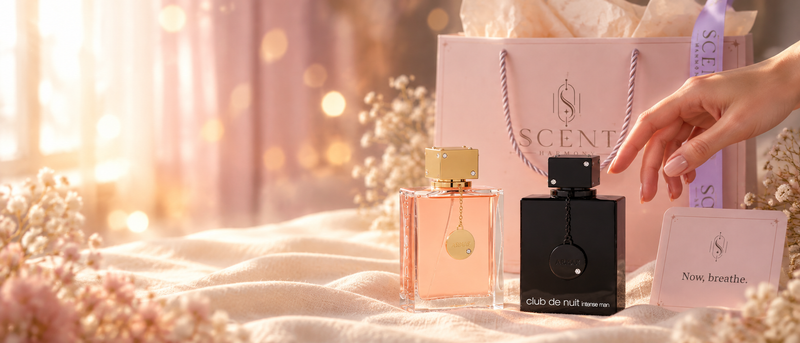 Una mano eligiendo entre dos perfumes, junto a la bolsa de regalo rosa de Scent Harmony.
