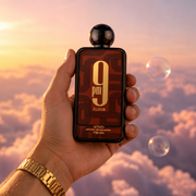 A hand holds the bottle of 9 PM Elixir by Afnan among pink clouds.