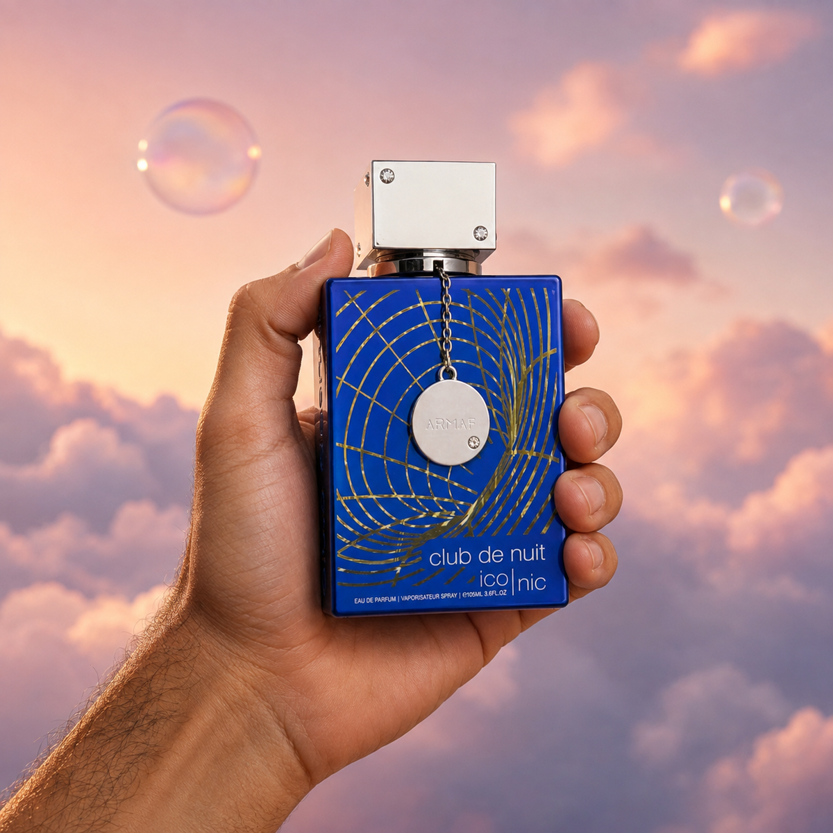 A hand holds the bottle of Club de Nuit Blue Iconic by Armaf among pink clouds.