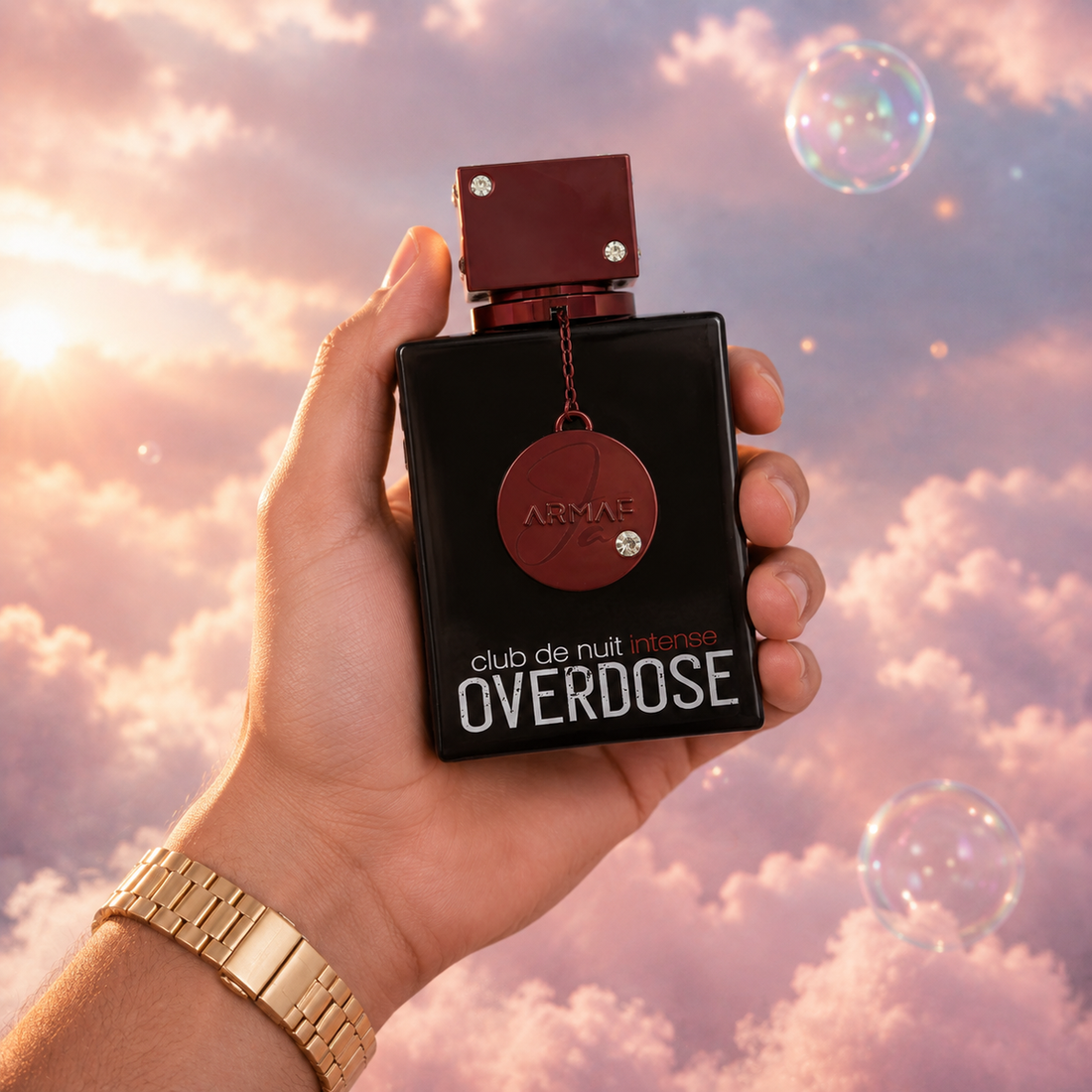 Una mano sostiene el frasco de Club de Nuit Intense Overdose de Armaf entre nubes rosadas.