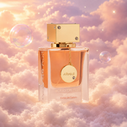 Frasco de Club de Nuit Woman Extrait de Parfum de Armaf sobre un banco de nubes, en un cielo rosa y lavanda con pompas iridiscentes y luz dorada.