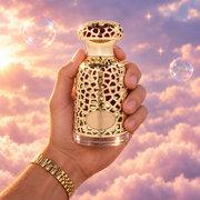 A hand holds the bottle of Emeer by Lattafa among pink clouds.