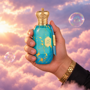 Una mano sostiene el frasco de Eter Arabian Sky de Armaf entre nubes rosadas.