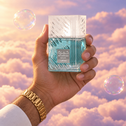 A hand holds the bottle of Khamrah Waha by Lattafa among pink clouds.