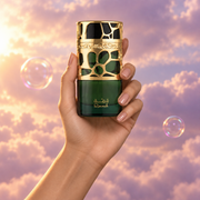 A hand holds the bottle of Qimmah by Lattafa among pink clouds.