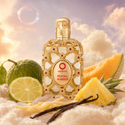The bottle of Royal Amber by Orientica surrounded by bergamot, green notes, melon and pineapple, on clouds.