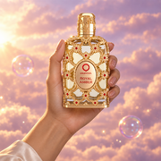 A hand holds the bottle of Royal Amber by Orientica among pink clouds.