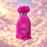 Bottle of Uhud by Arabiyat Prestige on a bank of clouds, in a pink and lavender sky with iridescent bubbles and golden light.