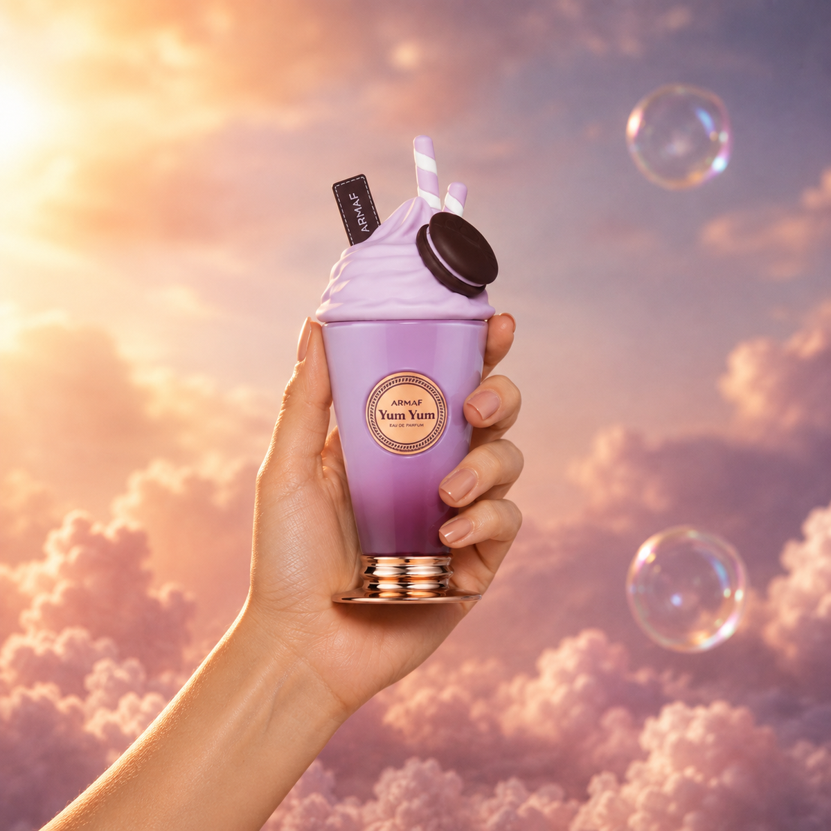 A hand holds the bottle of Yum Yum by Armaf among pink clouds.